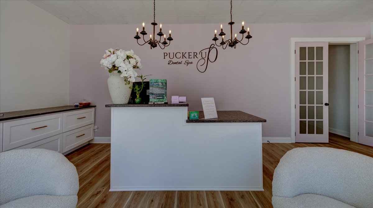 A dental office waiting room with light pink walls and chandeliers.