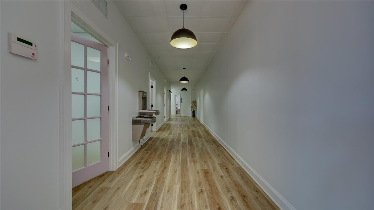 A dental office hallway with light wood floors and light pink doors.