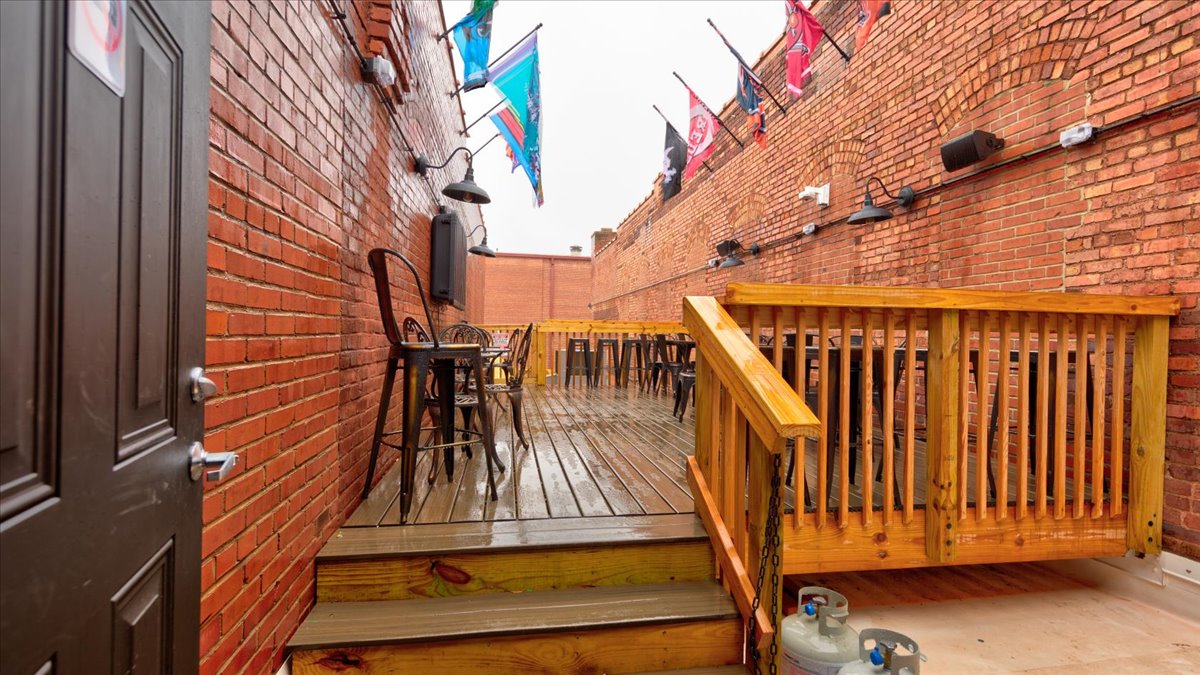 A wooden deck outside of a bar with brick walls. Includes sports flags.