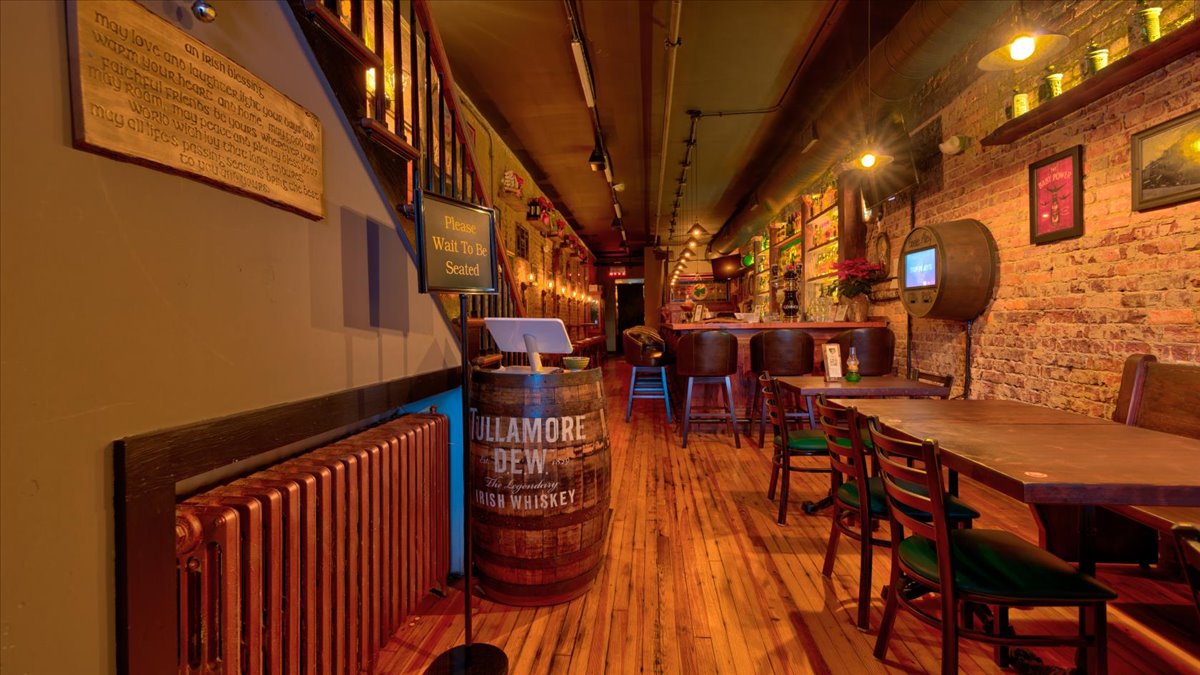 A row of wood tables in a dimly lit bar that has brick walls.