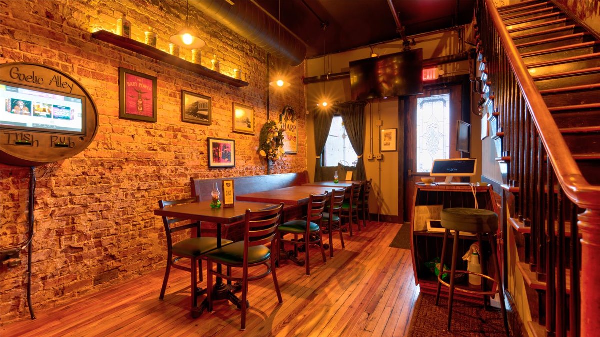 A row of wood tables in a dimly lit bar that has brick walls.