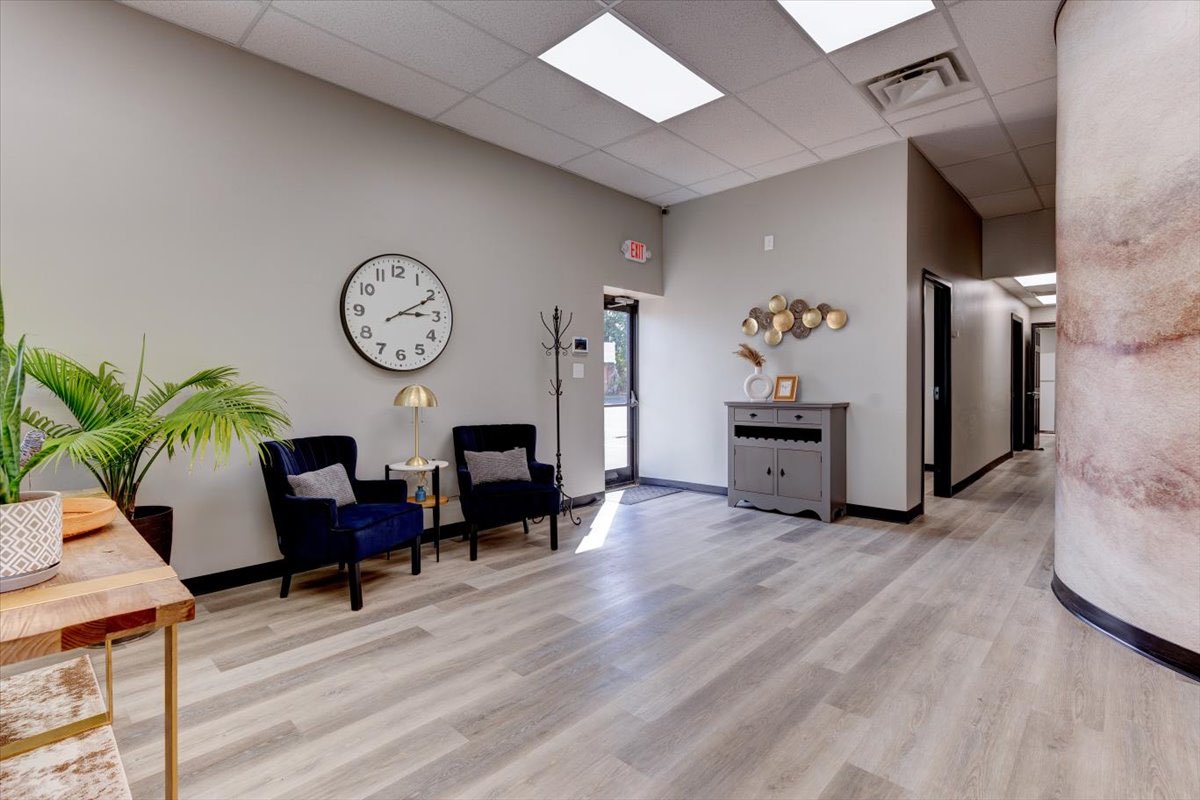 A modern office waiting room with two blue chairs and a large clock on the wall.