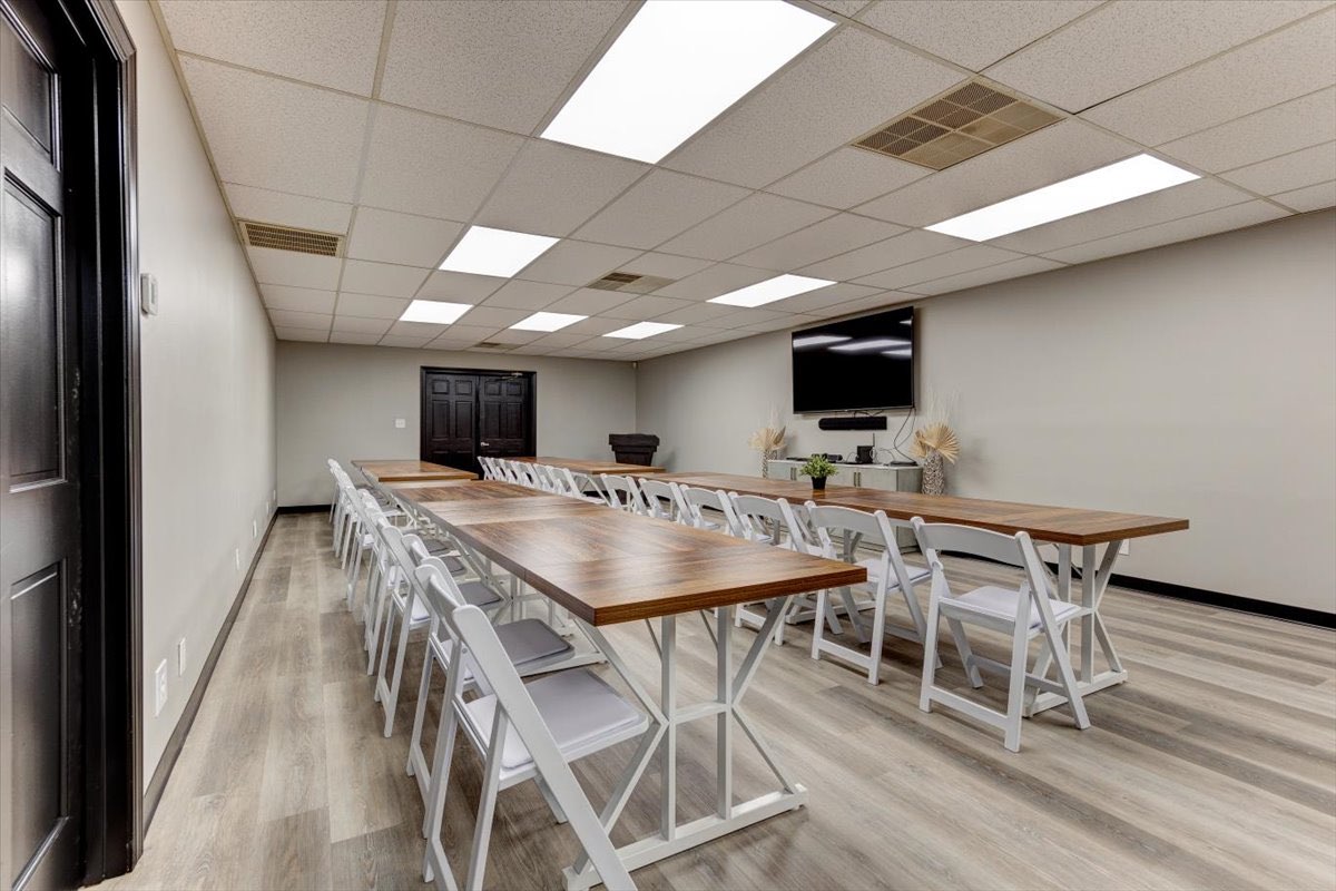 An office break room with two long tables, chairs and TV on the wall.