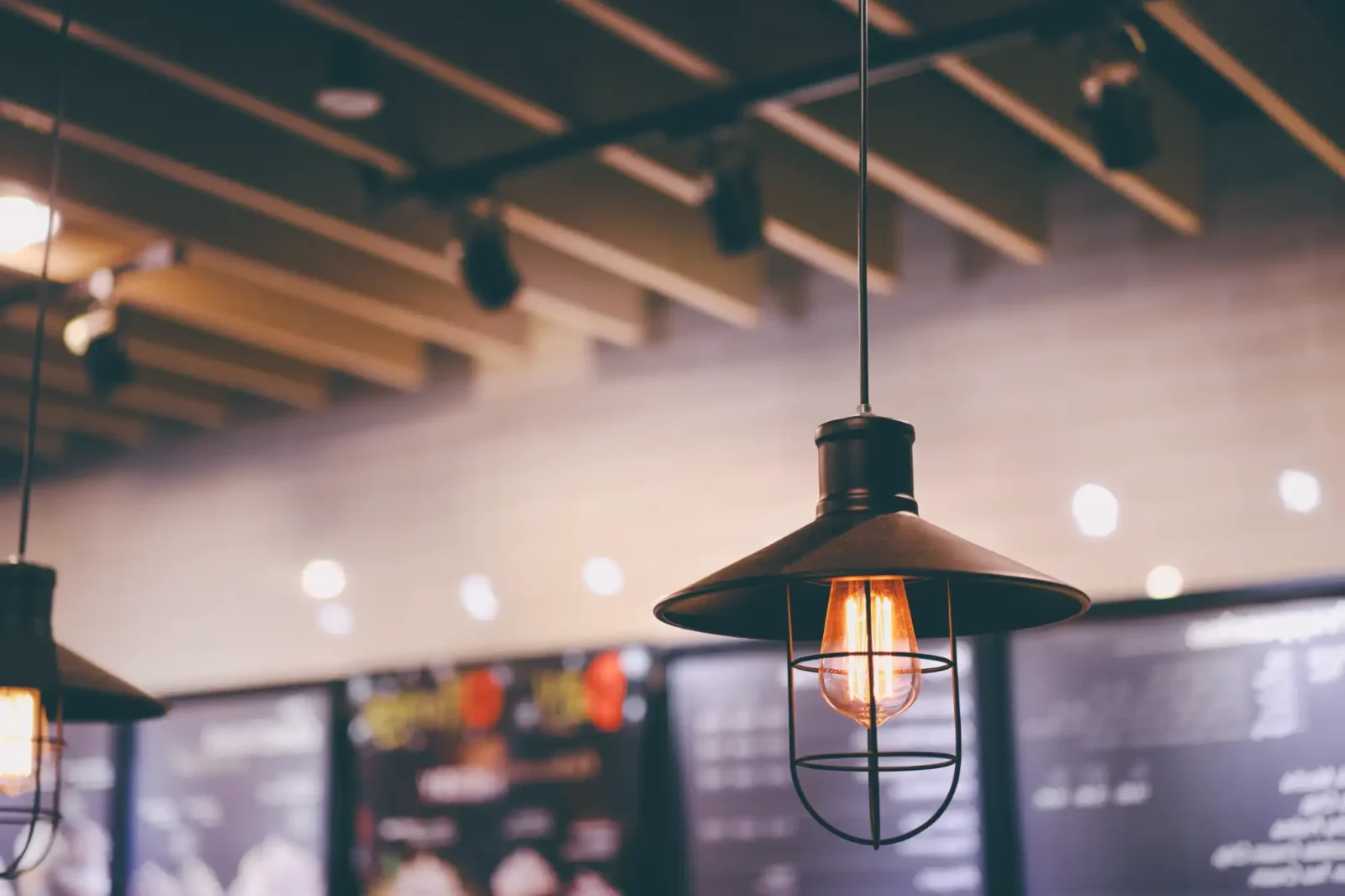 Edison lightbulb inside industrial light hanging from the ceiling in front of large restaurant menus