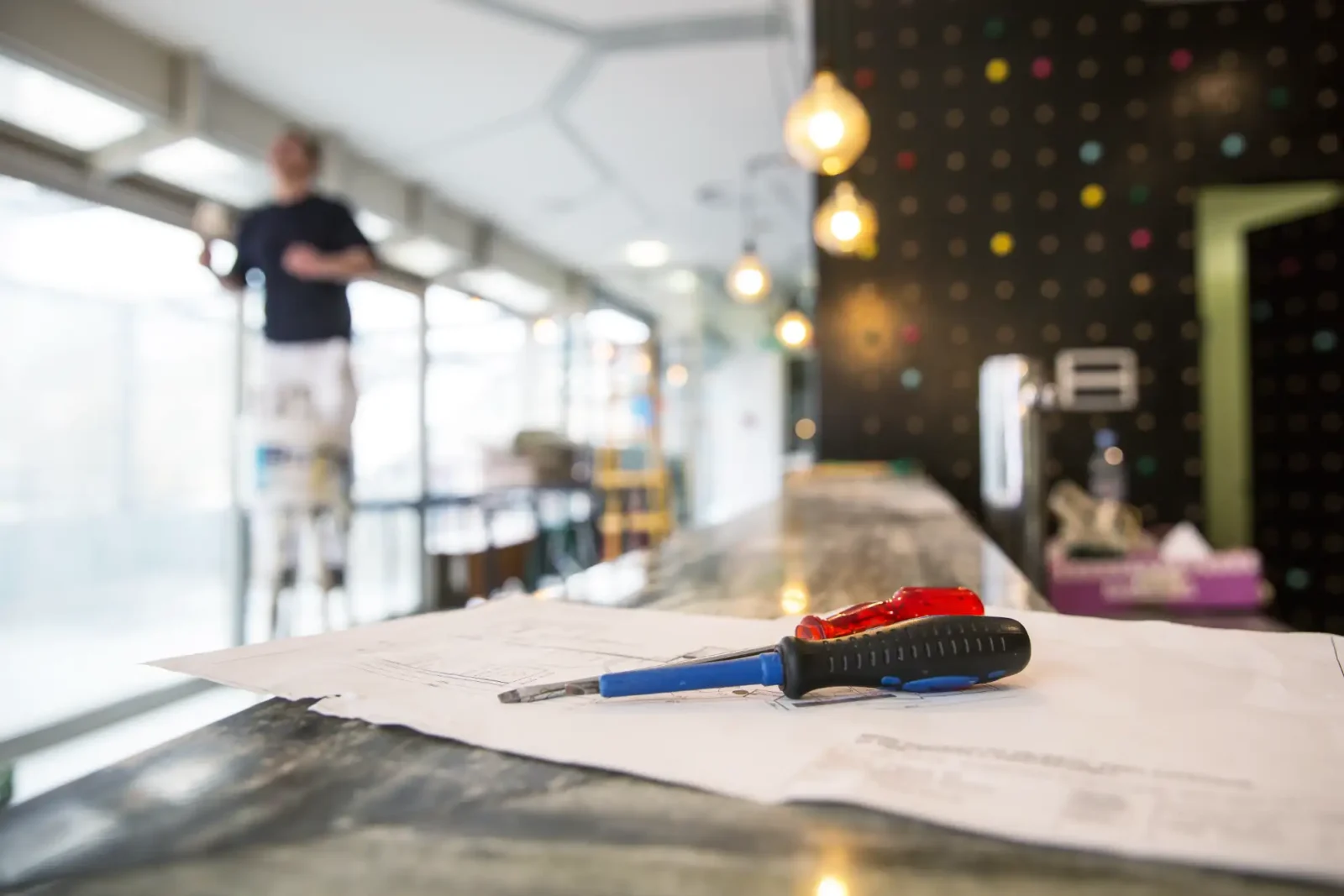 screwdrivers on a blueprint with a man working in a blurred background of a restaurant