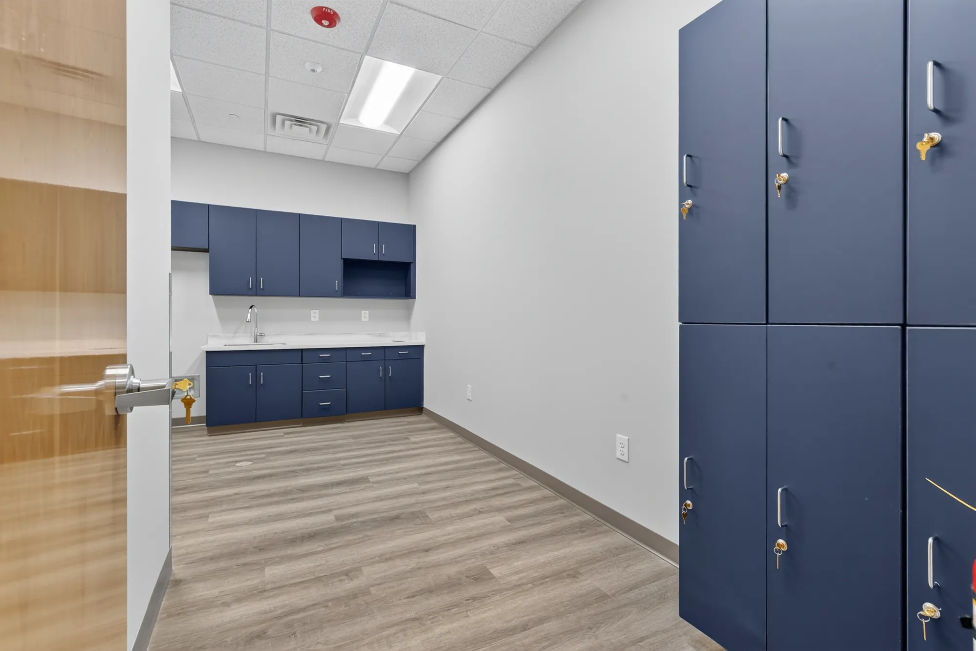 A clean, new utility room featuring navy blue cabinets with a sink and white counters, plus matching employee lockers along the right wall.