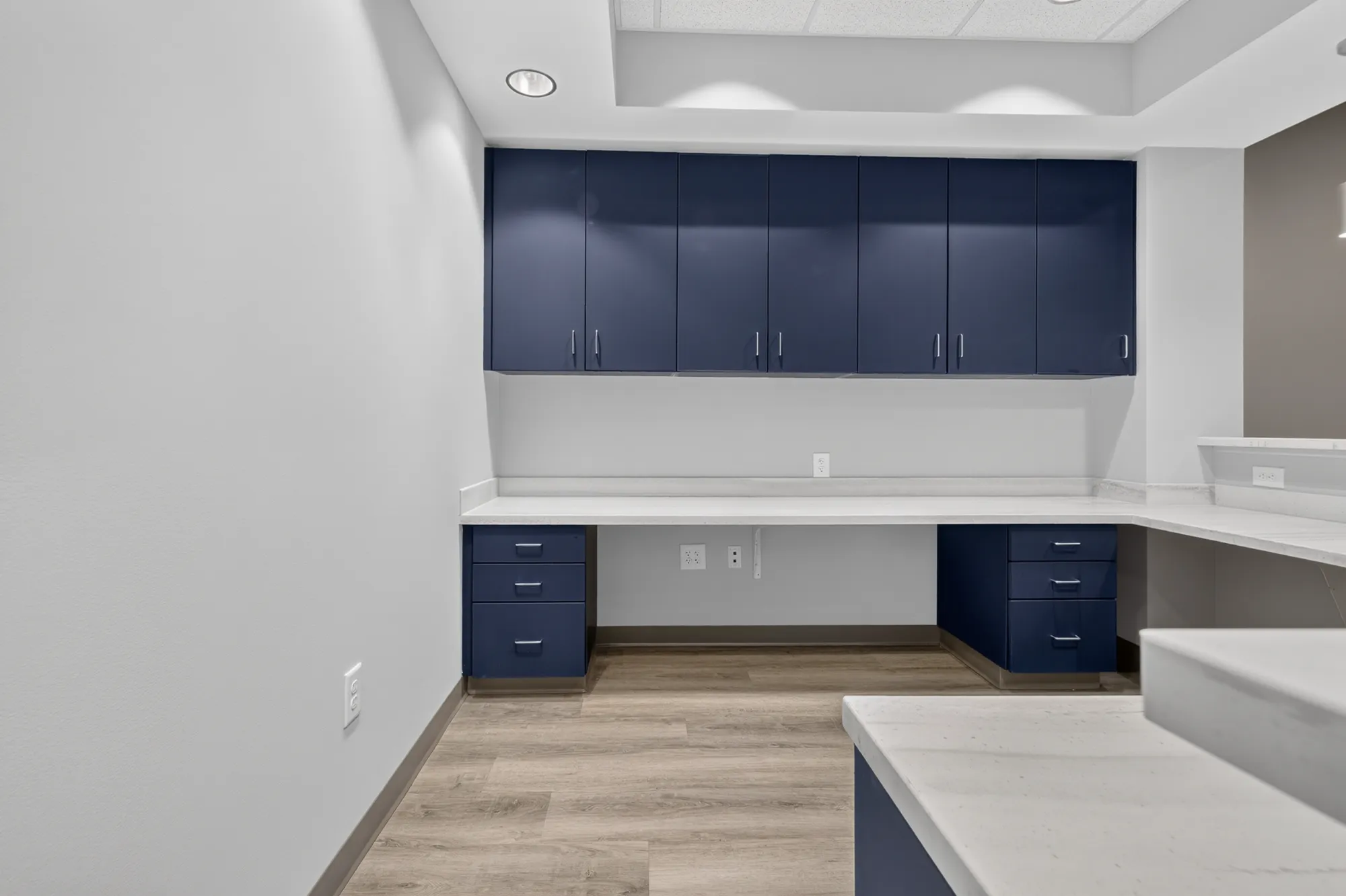 A custom built-in counter in a surgical office featuring navy blue cabinets and a white stone countertop above light wood flooring.